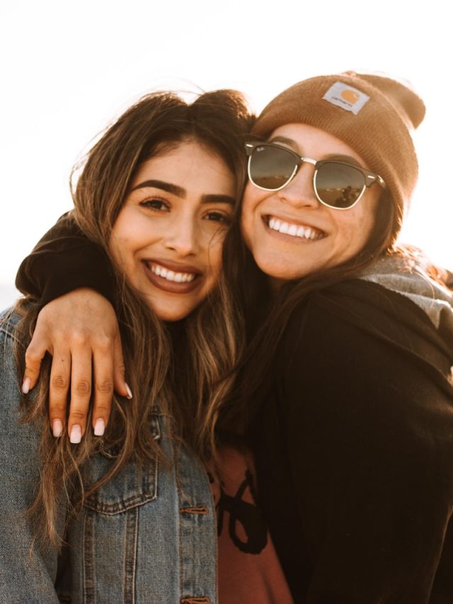 woman hugging other woman while smiling at beach