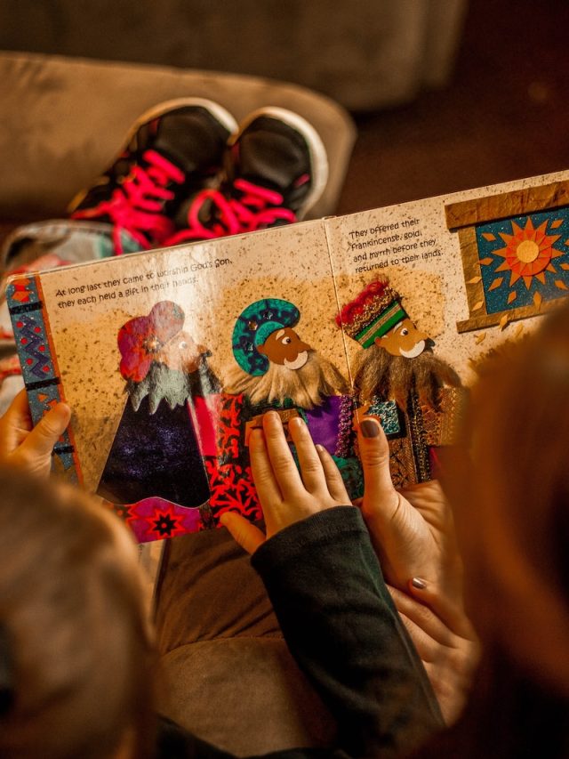 two childrens reading book while sitting on brown sofa